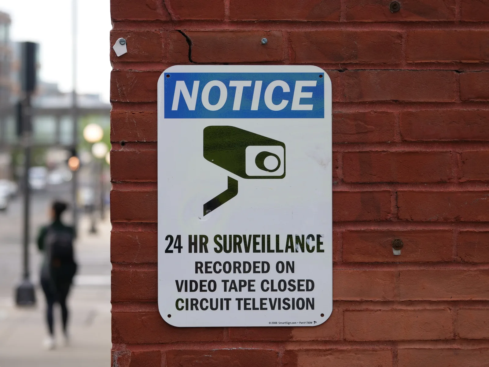 Close-up of a surveillance notice on a brick wall, urban setting.