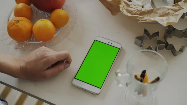Top view of a smartphone with a green screen next to a plate of oranges and an apple on a table. Four evidence designs for privacy first measurement in England, and what each gives up