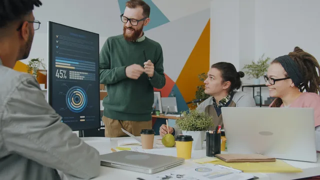 A diverse team engaged in a business meeting, analyzing company metrics on a presentation board. Privacy first measurement metrics: defining journey completion and reconciliation coverage
