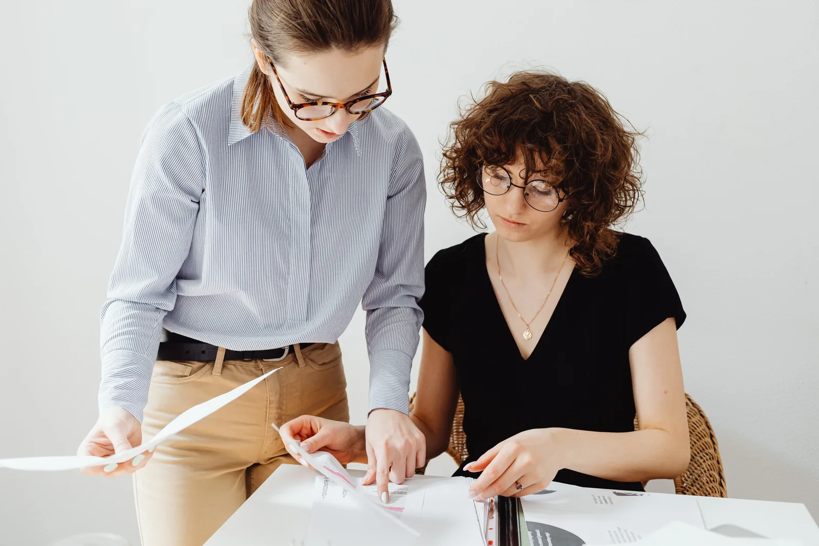 Two businesswomen reviewing documents at a workspace, focusing on collaboration and teamwork.