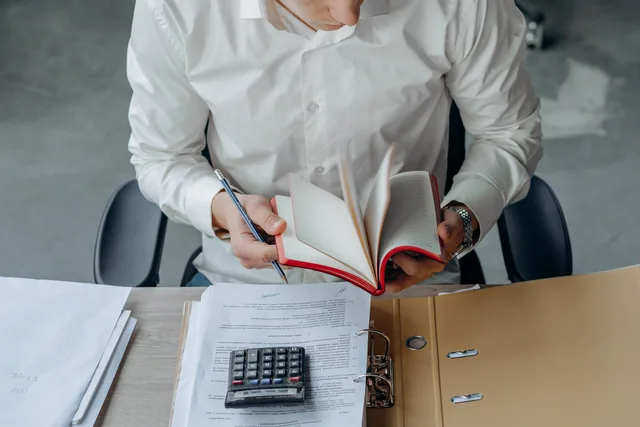 Man in white shirt reading book at office desk with calculator and documents. Planning measurement demand without inventing a growth rate