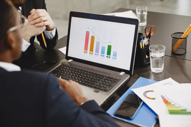 Two professionals analyzing a business graph on a laptop during a meeting. Reviewing measurement products and agencies without manufacturing a ranking